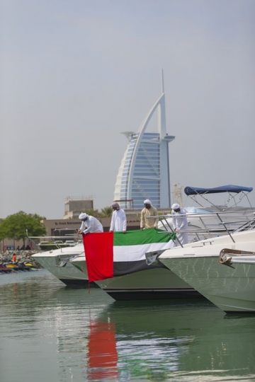 Arab men standing by the yacht with a background of a landmark celebrating National Day|