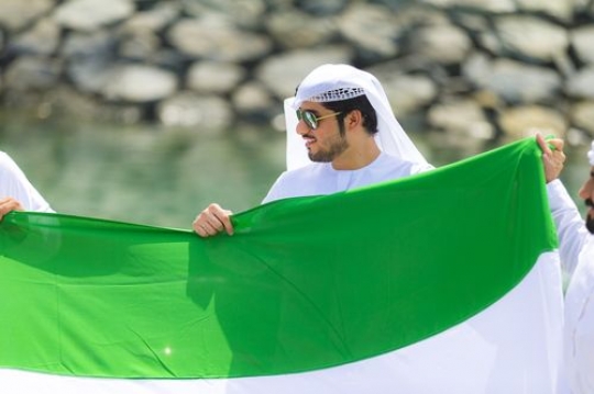 Arabian men dressed in the traditional attire holding a UAE Flag to represent their country during National Day|