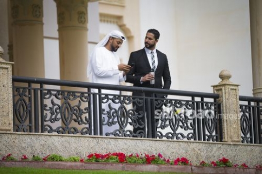 Middle Eastern Businessman using his mobile standing next to his colleague|-