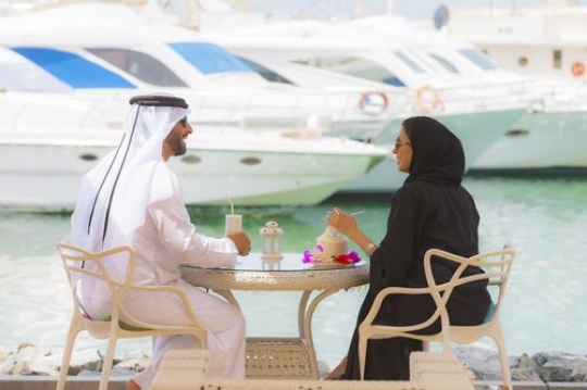 Arab woman and man dressed in the traditional UAE attire while sitting and talking to each other|