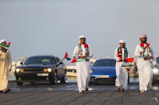 A group of men dressed in the UAE traditional attire followed by luxury cars at a National Day parade|