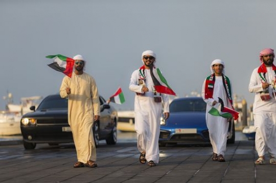 Family and friends representing their country followed by luxury cars during a national day parade|-