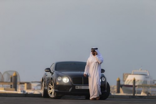 Middle eastern man dressed in the UAE traditional attire walking away from parked vehicle|-