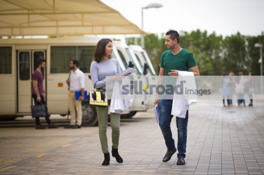 Middle Eastern man walking with the student together on campus|