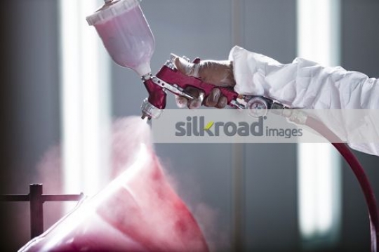 Worker spray painting the part of the car red|