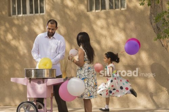Arab man and girl standing next to the cotton candy machine |-