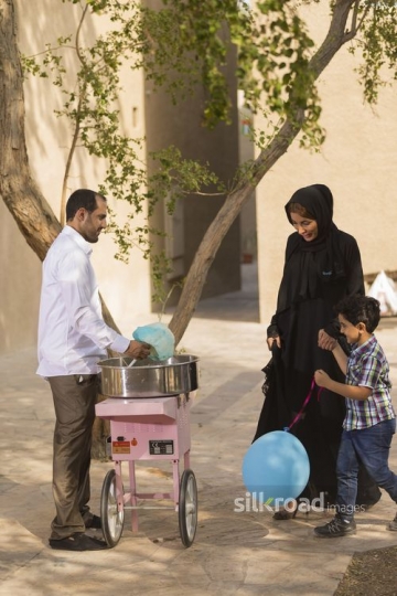 Arab mother and son walking towards the man making cotton candy|-