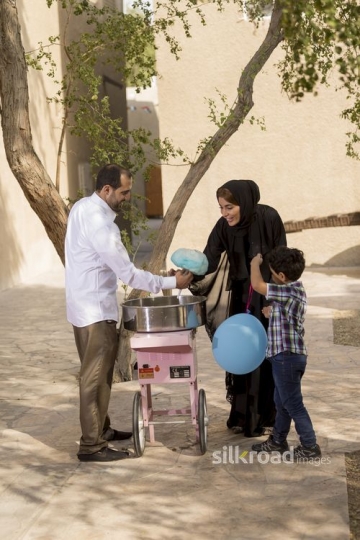 Middle Eastern man offering the mother and kids cotton candy|-