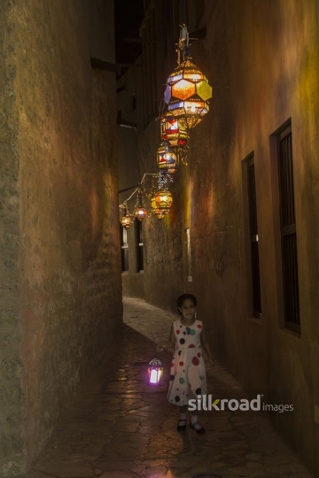 Arab girl running through the pathway decorated by Ramadan Lanterns|-