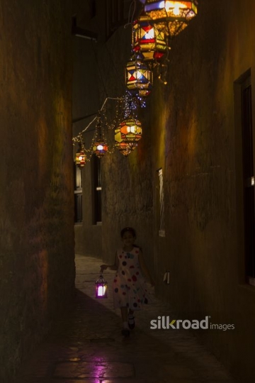 Arab girl running through the pathway decorated by Ramadan Lanterns|-