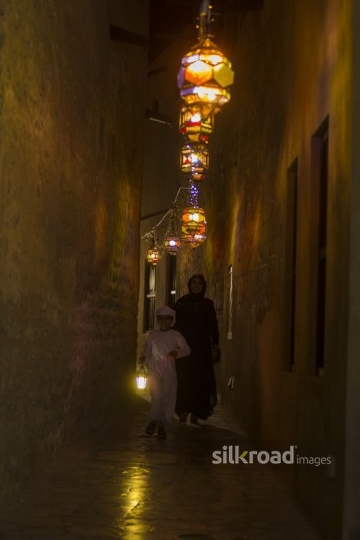 Arab boy walking in front of her mother carrying a Ramadan Lantern|-