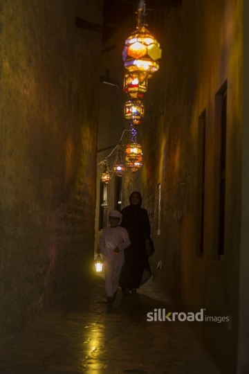 Arab mother walking behind her son carrying a Ramadan Lantern|-