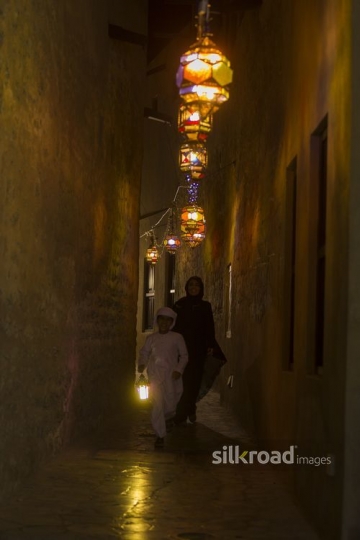 Arab woman walking behind her son carrying a Ramadan Lantern|-