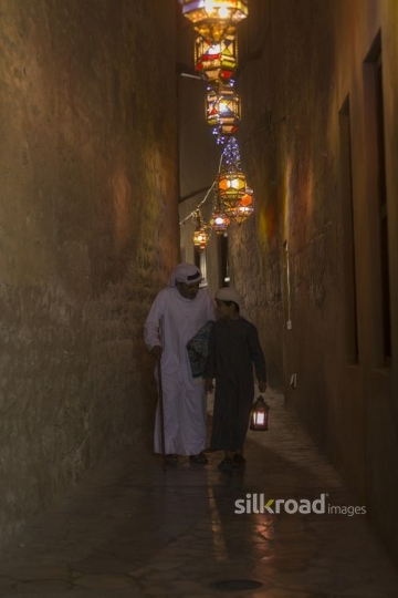 Middle Eastern father and son strolling through a lantern lit alleyway|-