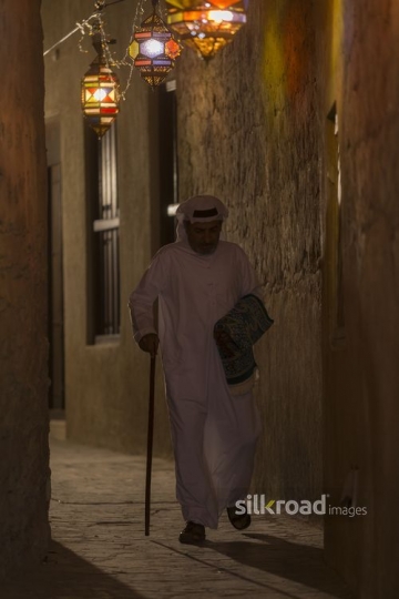 Middle eastern man strolling through an alleyway lit by Ramadan Lanterns