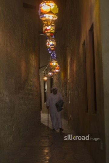 Middle Eastern man strolling through the alley carrying a prayer rug|-