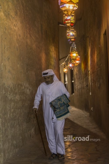 Arab man carrying the prayer rug while walking through the pathways of the Ramadan Lanterns|-