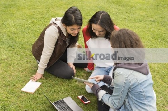 Women sitting together outside using device|