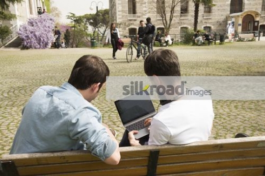 Men sitting together on the bench using the laptop