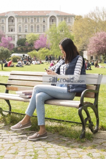 Student texting on her mobile sitting on the bench|