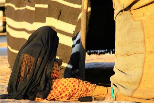 old woman in traditional custom sitting in front of a tent
