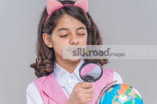 Arab kid looking at the globe through the magnifying glass|