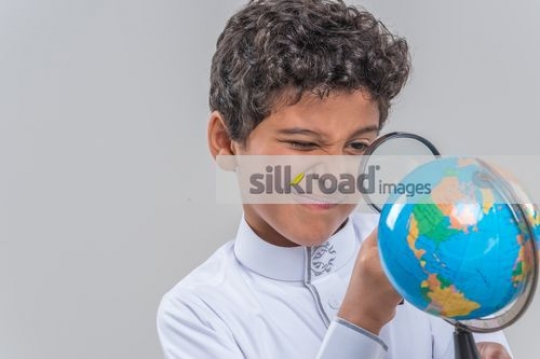 Young Middle Eastern kid using the magnifying glass|