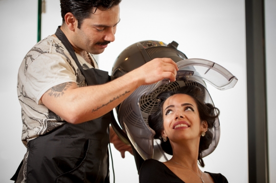 Hairdresser talking to his customer sitting under the blow drying machine|