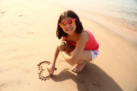 Little Girl Drawing A Heart In Sand