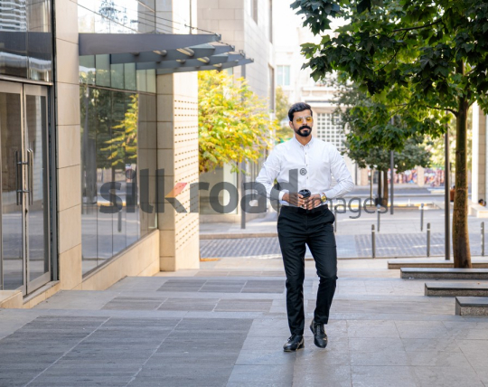 Man Walking Between Modern Buildings with Coffee Cup in Al Abdali Boulevard