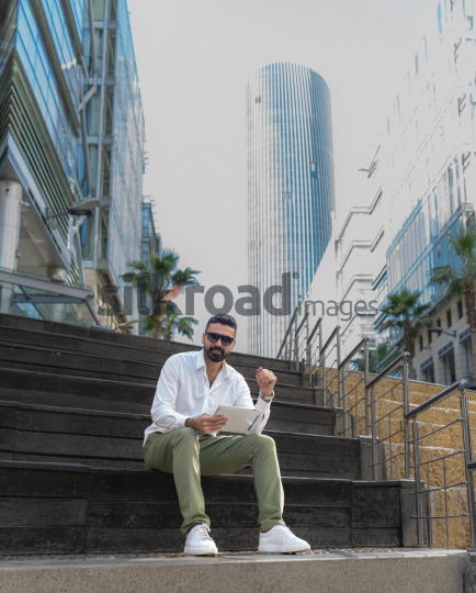 Man with Sunglasses Working on Laptop at Al Abdali Boulevard with Rotana Hotel Tower