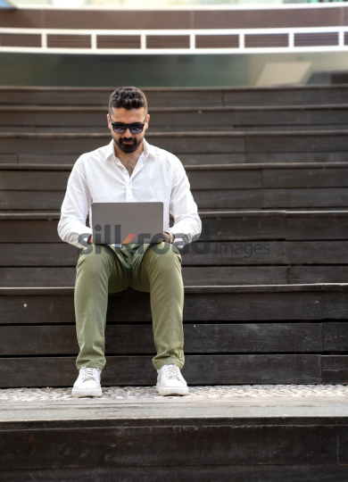 Man with Sunglasses Working on Laptop at Sunrise in Jordan’s Al Abdali Boulevard