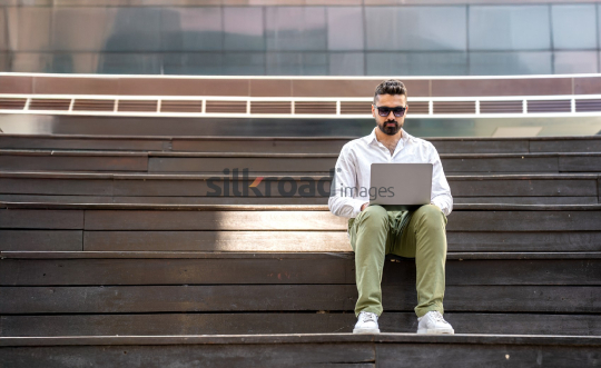 Man with Sunglasses Working on Laptop at Sunrise in Jordan’s Al Abdali Boulevard