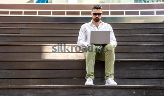Man with Sunglasses Working on Laptop at Sunrise in Jordan’s Al Abdali Boulevard