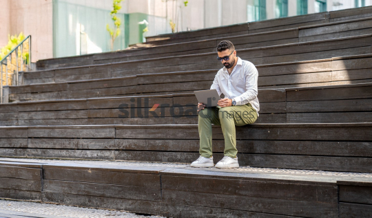 Man with Sunglasses Working on Laptop at Sunrise in Jordan’s Al Abdali Boulevard