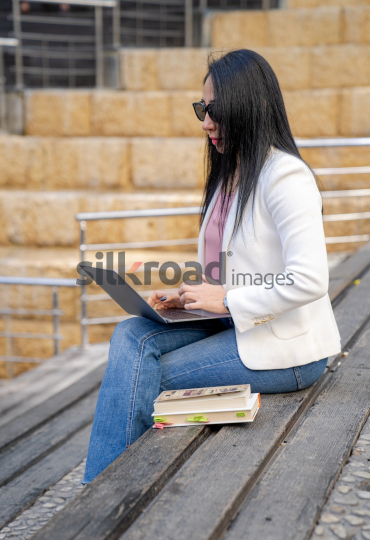 Professional Arab Woman Working with Laptop, Books, and Notebook in Jordan's Al Abdali Boulevard