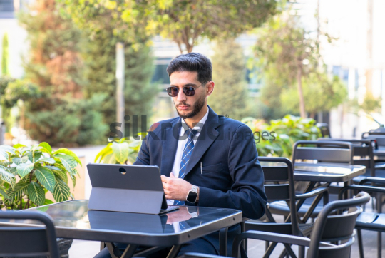 Professional Man in Suit and Sunglasses Preparing for Meeting on Laptop in Open Area on Amman Boulevard, Jordan