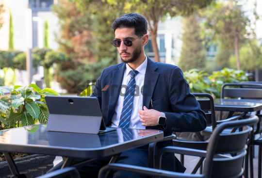 Professional Man in Suit and Sunglasses Preparing for Meeting on Laptop in Open Area on Amman Boulevard, Jordan