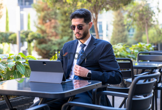 Professional Man in Suit and Sunglasses Preparing for Meeting on Laptop in Open Area on Amman Boulevard, Jordan