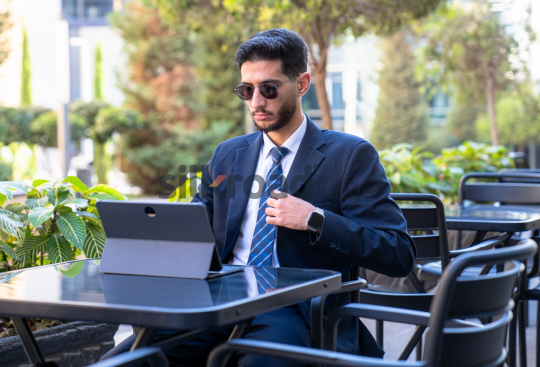 Professional Man in Suit and Sunglasses Preparing for Meeting on Laptop in Open Area on Amman Boulevard, Jordan