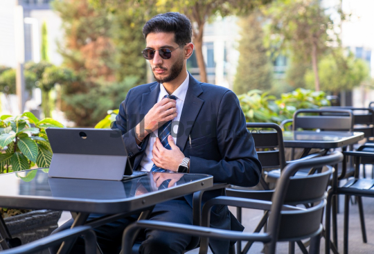 Professional Man in Suit and Sunglasses Preparing for Meeting on Laptop in Open Area on Amman Boulevard, Jordan