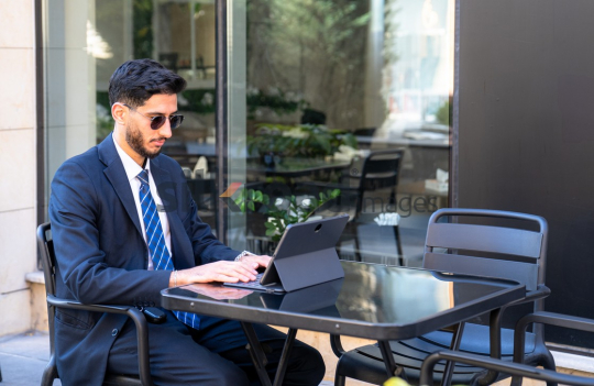 Professional Man in Suit with Sunglasses Working on Laptop in Open Area on Amman Boulevard, Jordan