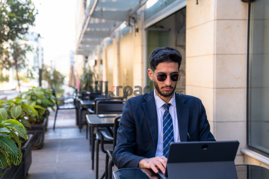 Professional Man in Suit with Sunglasses Working on Laptop in Open Area on Amman Boulevard, Jordan