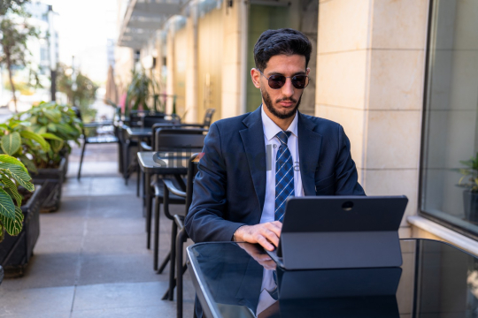 Professional Man in Suit with Sunglasses Working on Laptop in Open Area on Amman Boulevard, Jordan