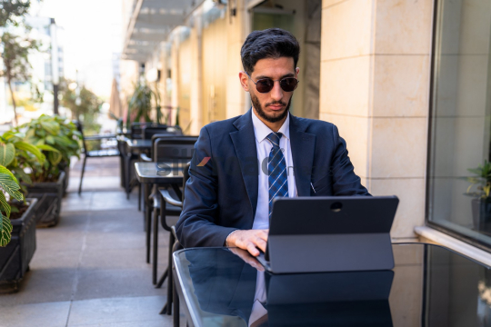 Professional Man in Suit with Sunglasses Working on Laptop in Open Area on Amman Boulevard, Jordan