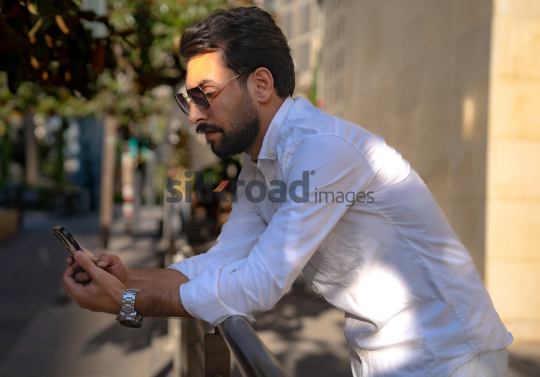 Professional Man Relaxing on Fence Checking Phone at Al Abdali Boulevard