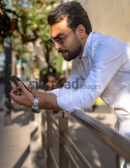 Professional Man Relaxing on Fence Checking Phone at Al Abdali Boulevard