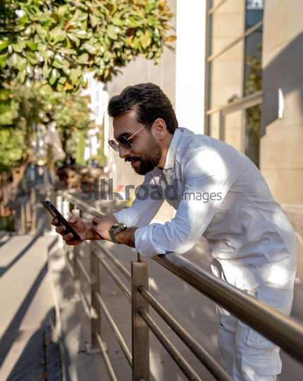 Professional Man Relaxing on Fence Checking Phone at Al Abdali Boulevard