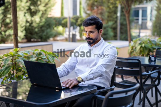Professional Man Working on Laptop at Desk in Open Area on Amman Boulevard, Jordan