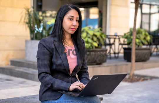 professional woman, working on laptop, Al Abdali Boulevard, problem-solving, focused expression, outdoor workspace, urban lifestyle, modern professional, thinking and working, Amman scenery.